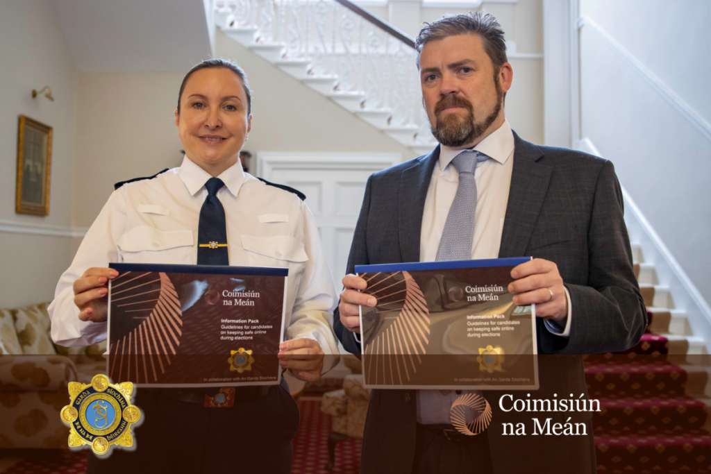 John Evans, Digital services Commissioner, standing with a representative of an Garda Síochána. Both are holding the Information Pack prepared jointly for the elections.